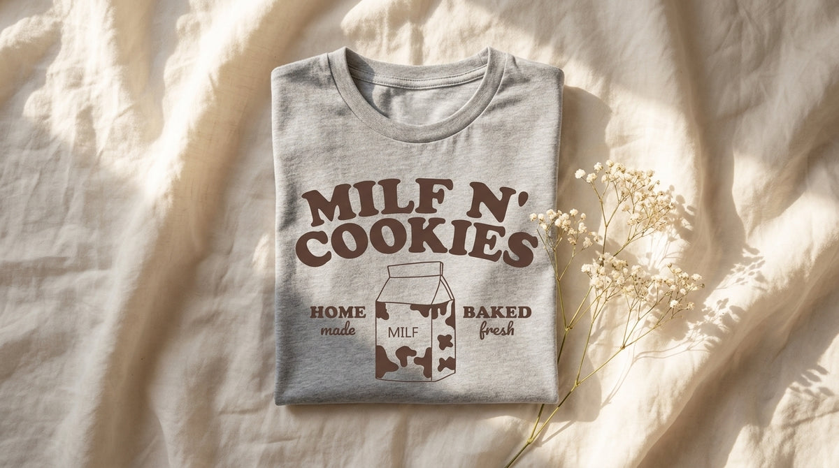 MILF N' Cookies graphic tee neatly folded on rumpled ivory linen with baby's breath sprig and window light, Peachy Journal lifestyle flat lay