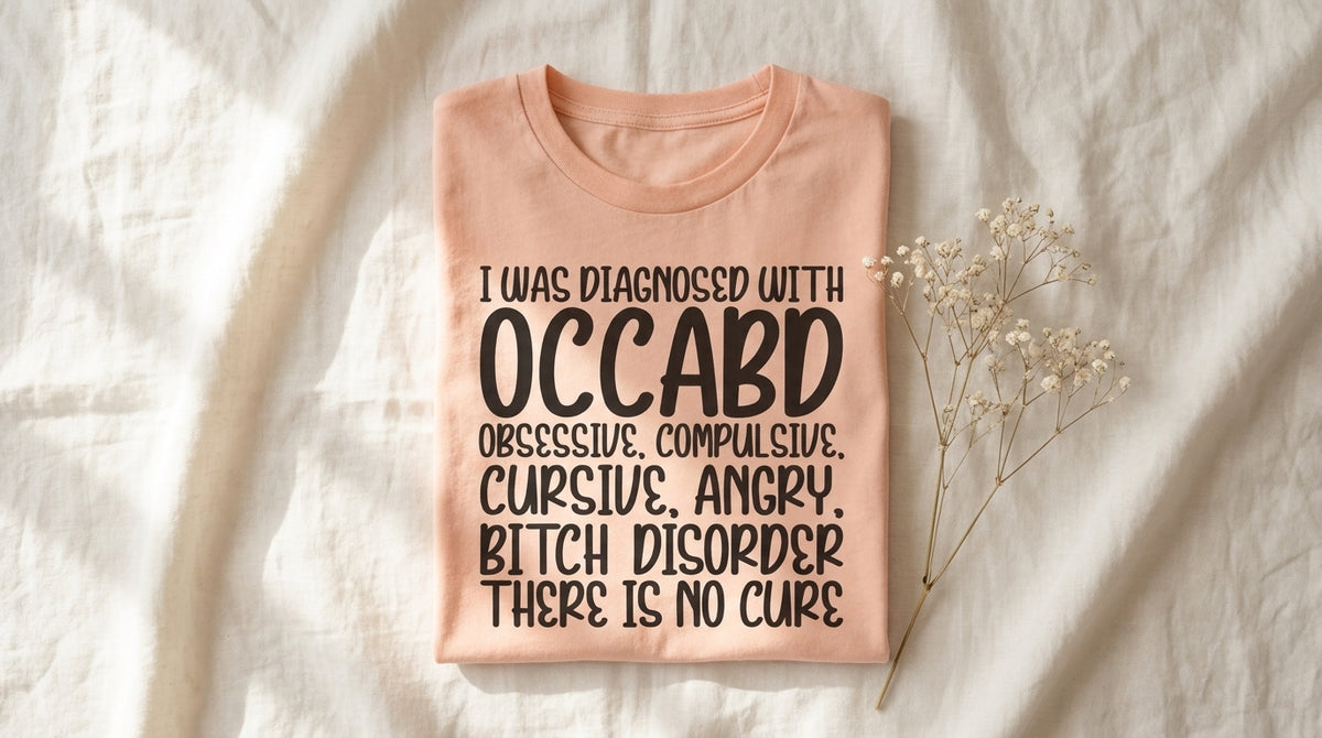 Folded peach I Was Diagnosed With OCCABD tee on rumpled ivory linen with baby's breath sprig – Peachy Sunday Journal featured hero