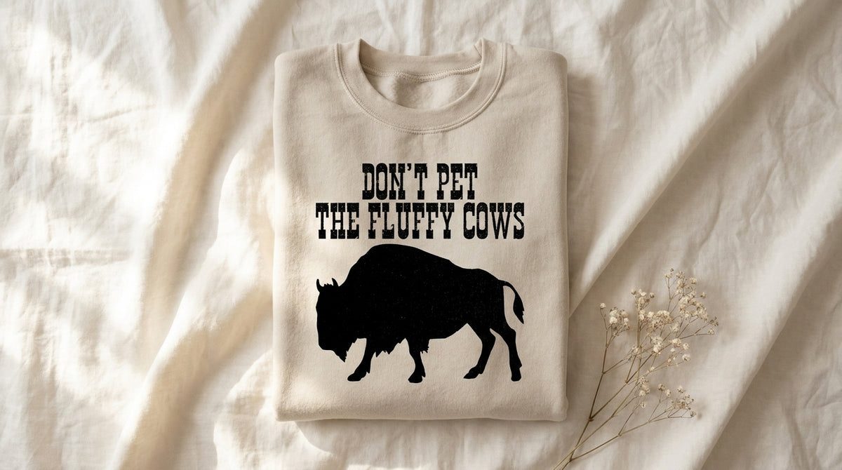 Folded sand Don't Pet The Fluffy Cows sweatshirt on rumpled ivory linen with dried baby's breath sprig – Peachy Sunday Journal national park wildlife humor