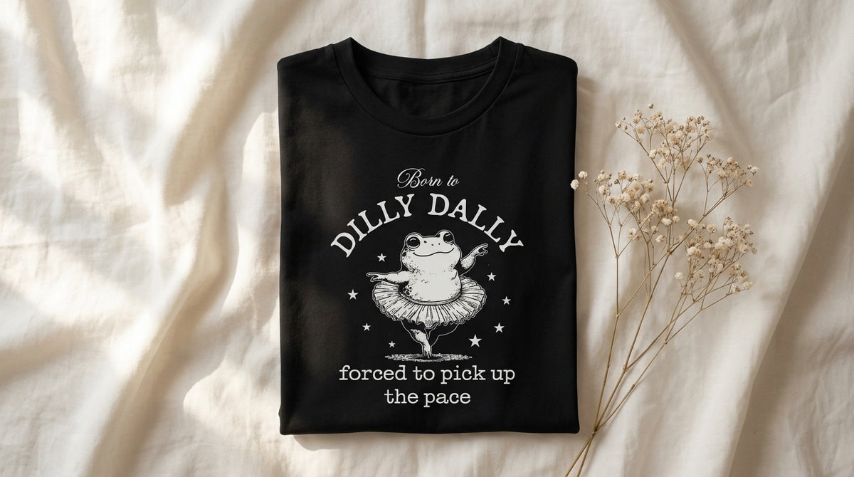 Folded black Born To Dilly Dally tee on rumpled ivory linen with baby's breath sprig – Peachy Sunday Journal featured hero
