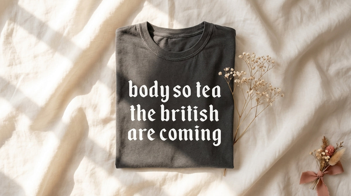 Garment-dyed pepper Body So Tea The British Are Coming tee folded on rumpled ivory linen with baby's breath sprig – Peachy Sunday Journal featured hero