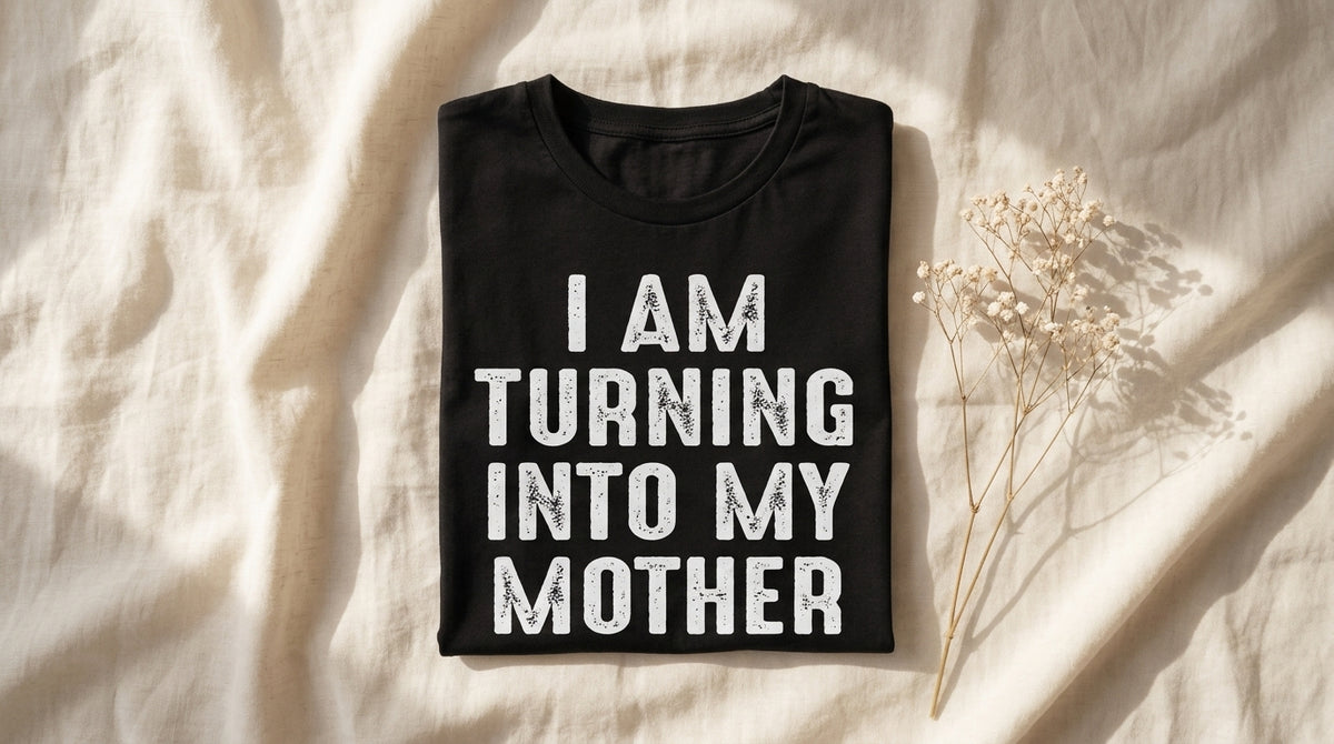 Folded black I Am Turning Into My Mother graphic tee on rumpled ivory linen with baby's breath sprig – Peachy Sunday mother daughter lifestyle article