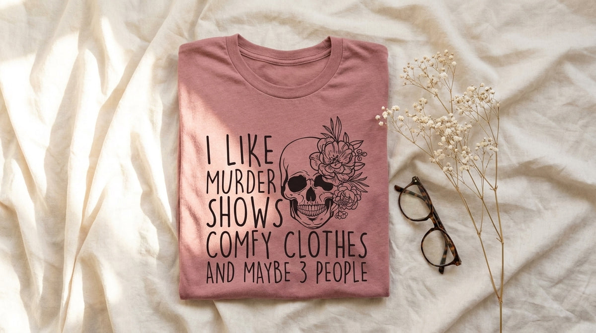 Folded mauve I Like Murder Shows Comfy Clothes and Maybe 3 People tee on rumpled ivory linen with baby's breath sprig and reading glasses – Peachy Sunday Journal featured hero