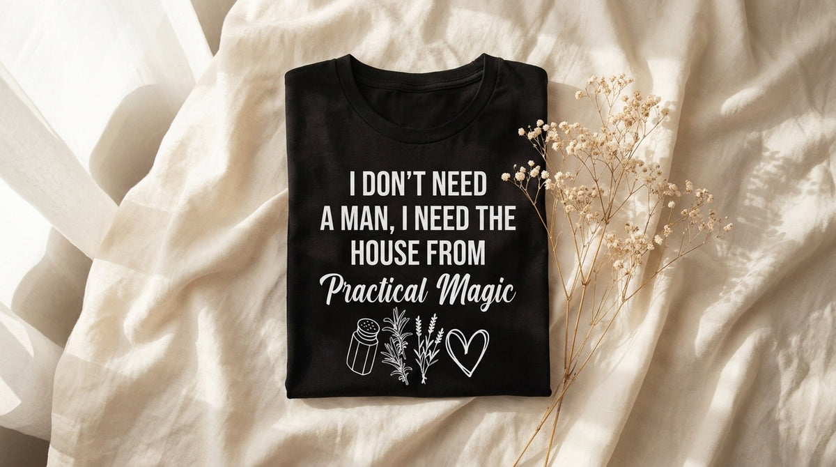 Folded black I Don't Need A Man I Need The House From Practical Magic tee on rumpled ivory linen with baby's breath sprig – Peachy Sunday Journal featured hero