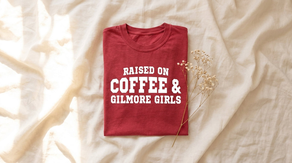 Folded crimson Raised On Coffee & Gilmore Girls tee on rumpled ivory linen with baby's breath sprig – Peachy Sunday Journal featured hero