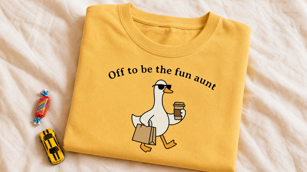 Mustard Off To Be The Fun Aunt graphic tee with candy and toy car on cream linen, UGC flat lay