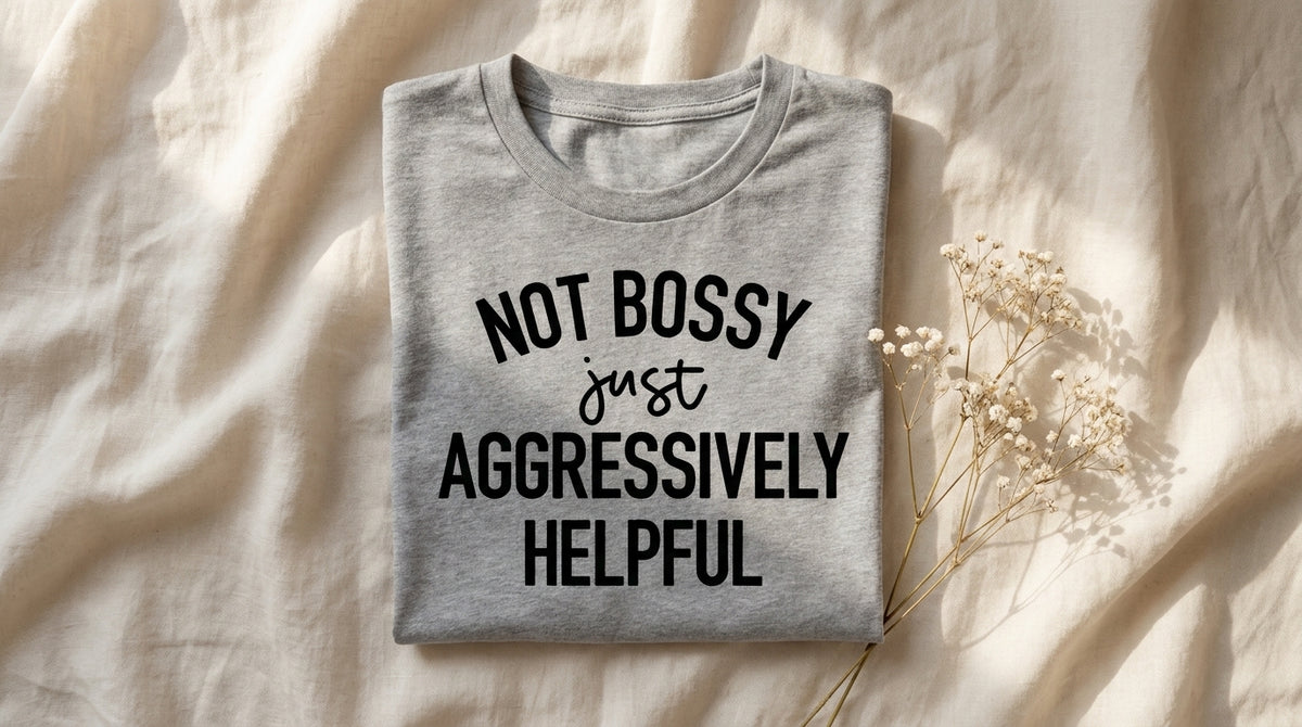 Folded heather grey Not Bossy Just Aggressively Helpful t-shirt on ivory linen with dried baby's breath – Peachy Sunday work humor survival guide