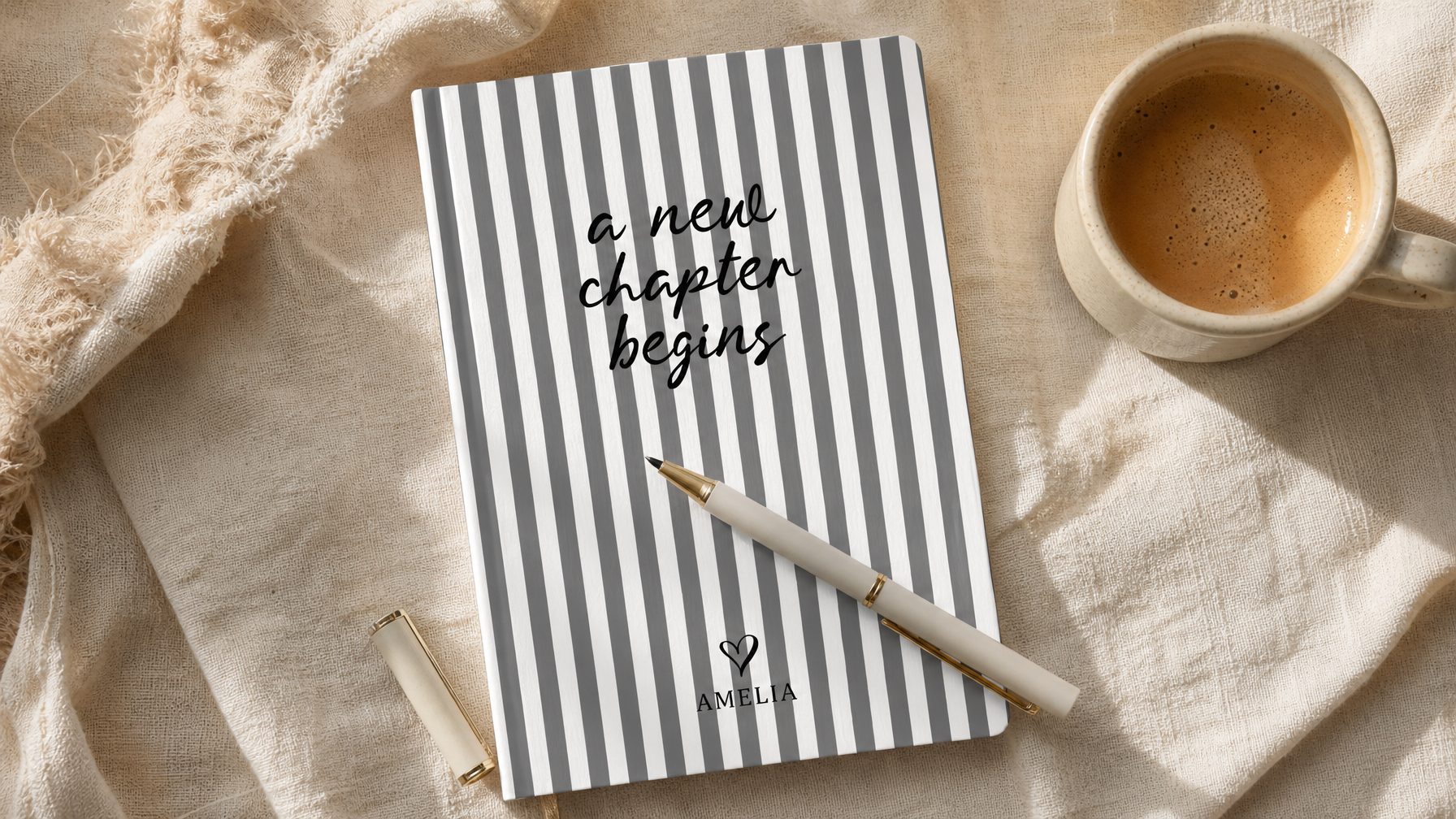 Personalized New Chapter Begins journal with an uncapped pen and coffee mug on warm cream linen, UGC flat lay new job gift