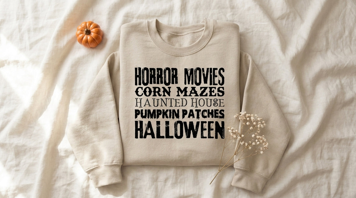 Horror Movies Corn Mazes Haunted House Pumpkin Patches Halloween Sweatshirt in sand folded on ivory linen with autumn baby's breath and mini pumpkin