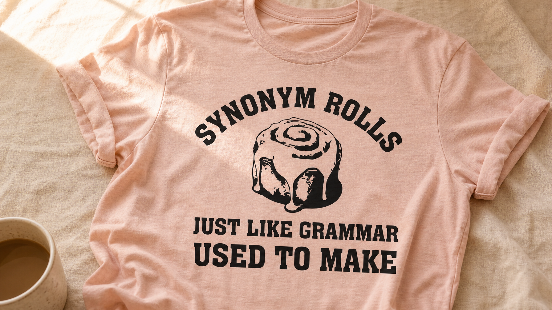 Synonym Rolls Just Like Grammar Used To Make Tee in heather prism peach flat-laid on a warm wooden desk with a steaming coffee mug and red grading pen – funny teacher gift idea from Peachy Sunday