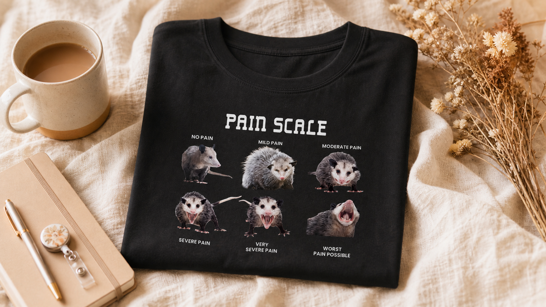 Nurse Pain Scale graphic tee flat-laid on cream linen with coffee mug, notebook, and badge reel – funny nurse gift idea from Peachy Sunday