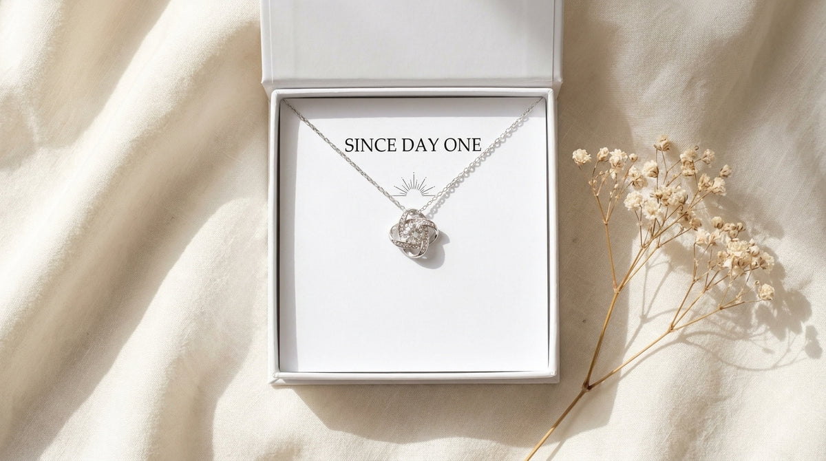 Since Day One Best Friend Love Knot Necklace in white gift box on rumpled ivory linen with baby's breath sprig, Peachy Sunday Journal flat lay