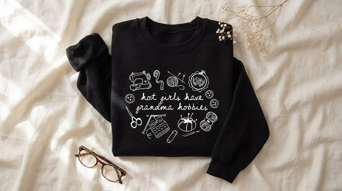 Hot girls have grandma hobbies black sweatshirt flat lay on rumpled ivory linen with baby's breath and reading glasses