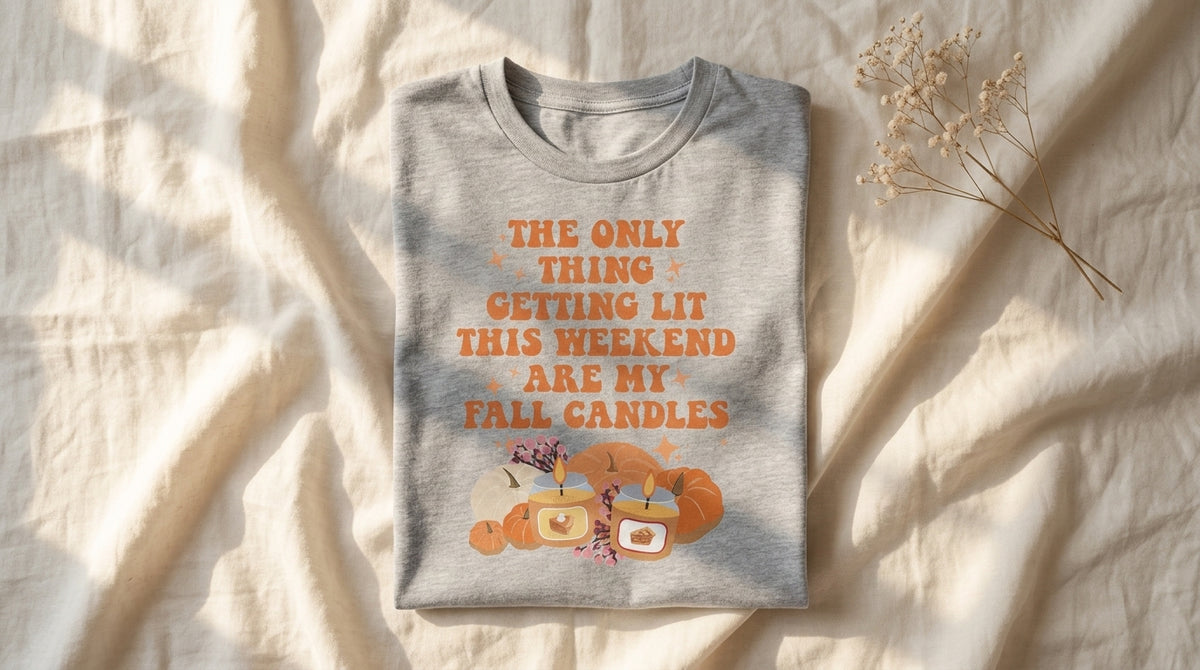 Folded grey The Only Thing Getting Lit This Weekend Are My Fall Candles tee on ivory linen with dried baby's breath sprig