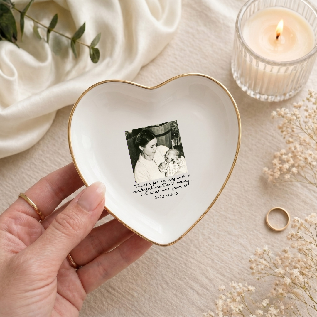 Heart-shaped trinket dish with a photo and text, held by a hand, on a soft background with flowers and a candle.